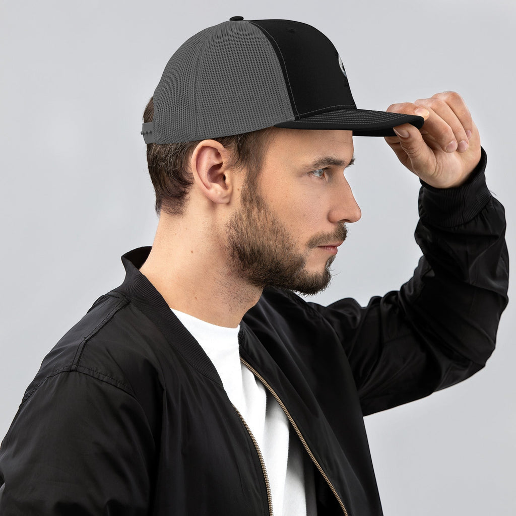 Stylio black and grey trucker cap with curved visor and mesh back, worn by a man.