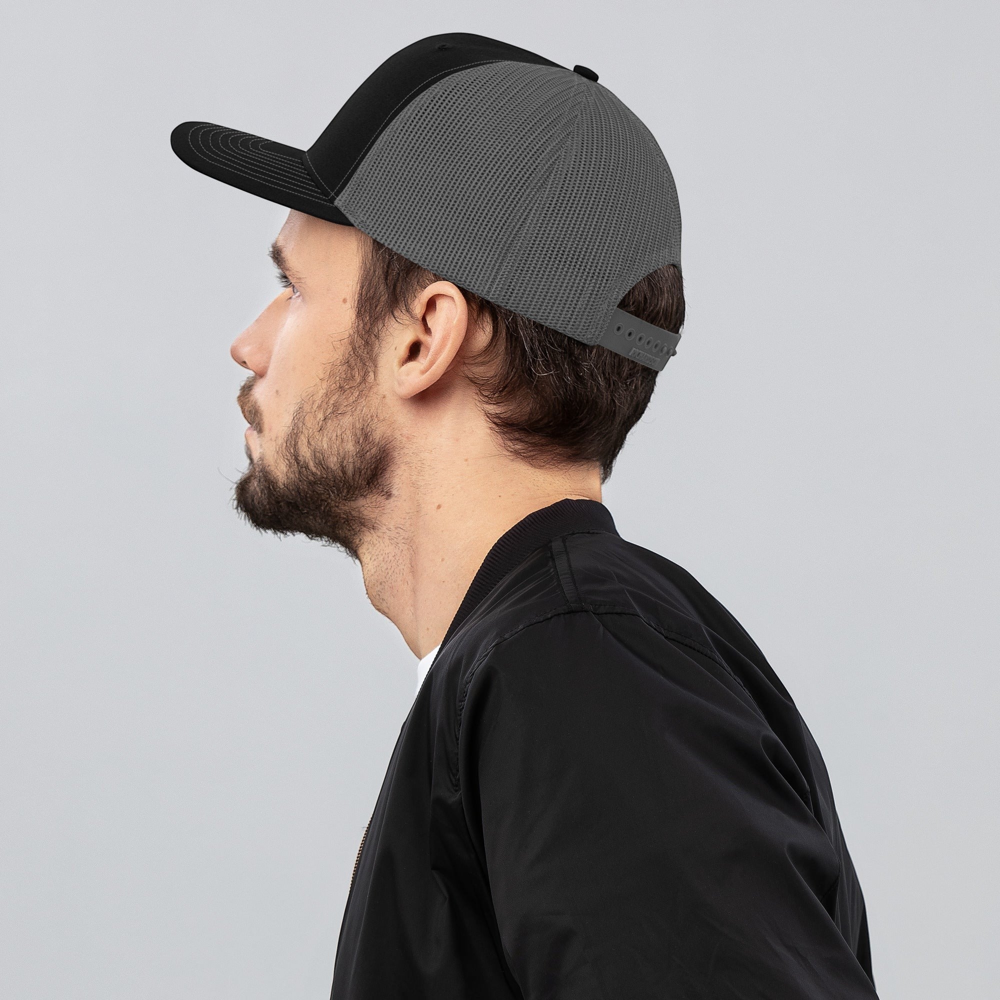 Stylio black and grey trucker cap with mesh back and curved visor worn by a man.