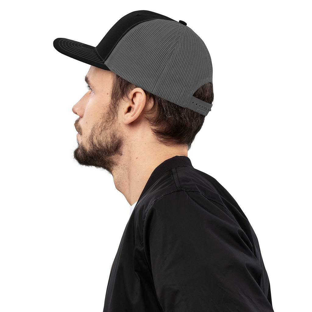 Stylio black and grey trucker cap with mesh back and curved visor, worn by a man.