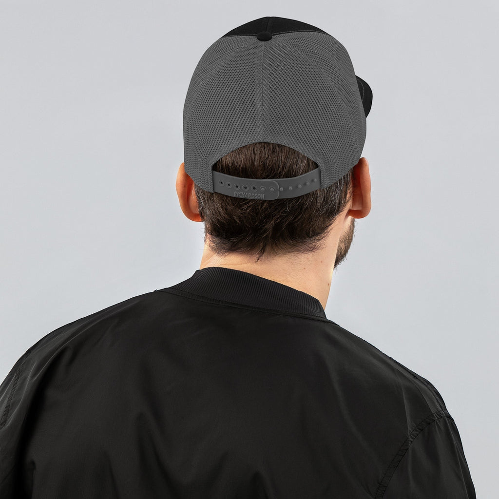 Stylio black and grey trucker cap with mesh back and adjustable snapback worn by a man.
