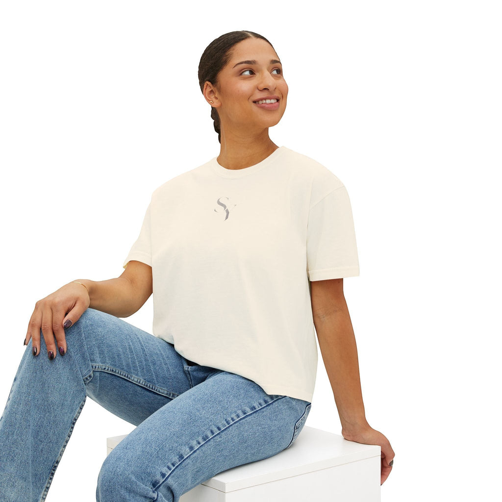 Stylio cream pigment-dyed cotton boxy tee with a subtle grey logo on the chest, worn by a woman with blue jeans.