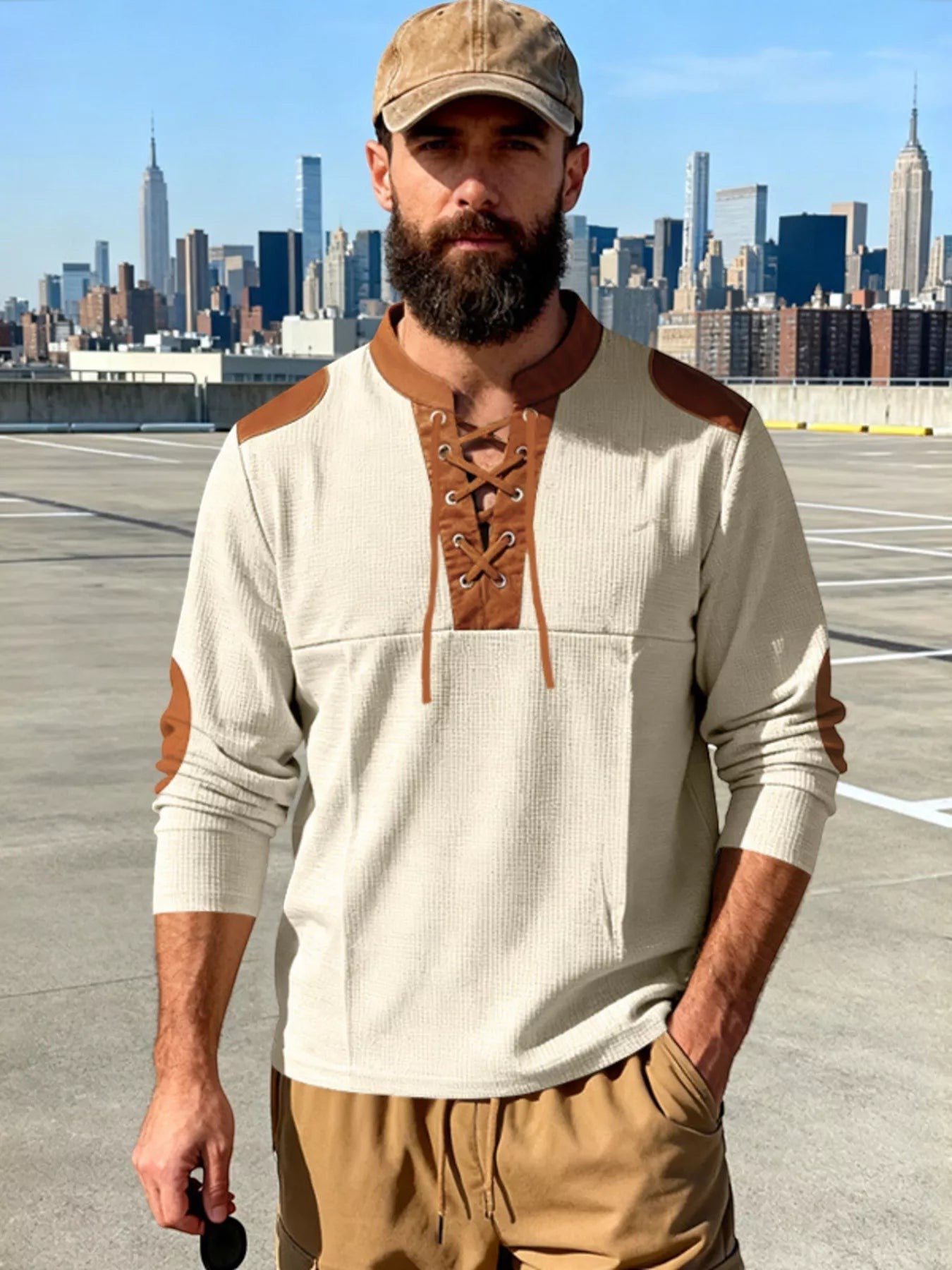 Stylio men's cream waffle knit long sleeve t-shirt with brown lace-up neckline and elbow patches. Model wears a tan baseball cap and tan cargo pants.
