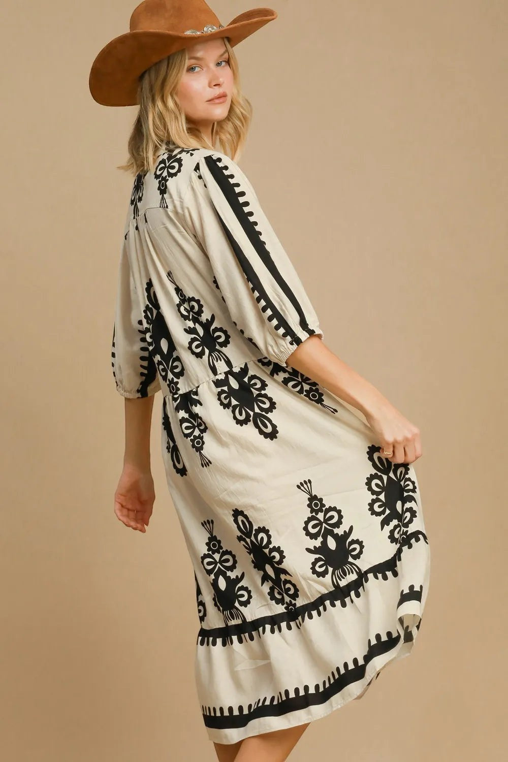 Stylio cream midi dress with black floral print, ruffled hem, and 3/4 sleeves. Model wears a brown cowboy hat.