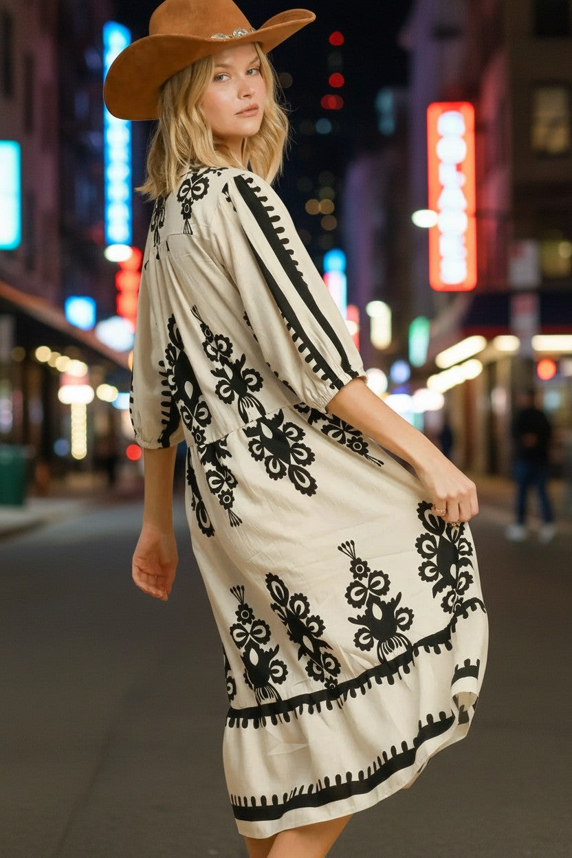 Stylio cream midi dress with black floral print, ruffled hem, and 3/4 sleeves. Model wears a brown cowboy hat.