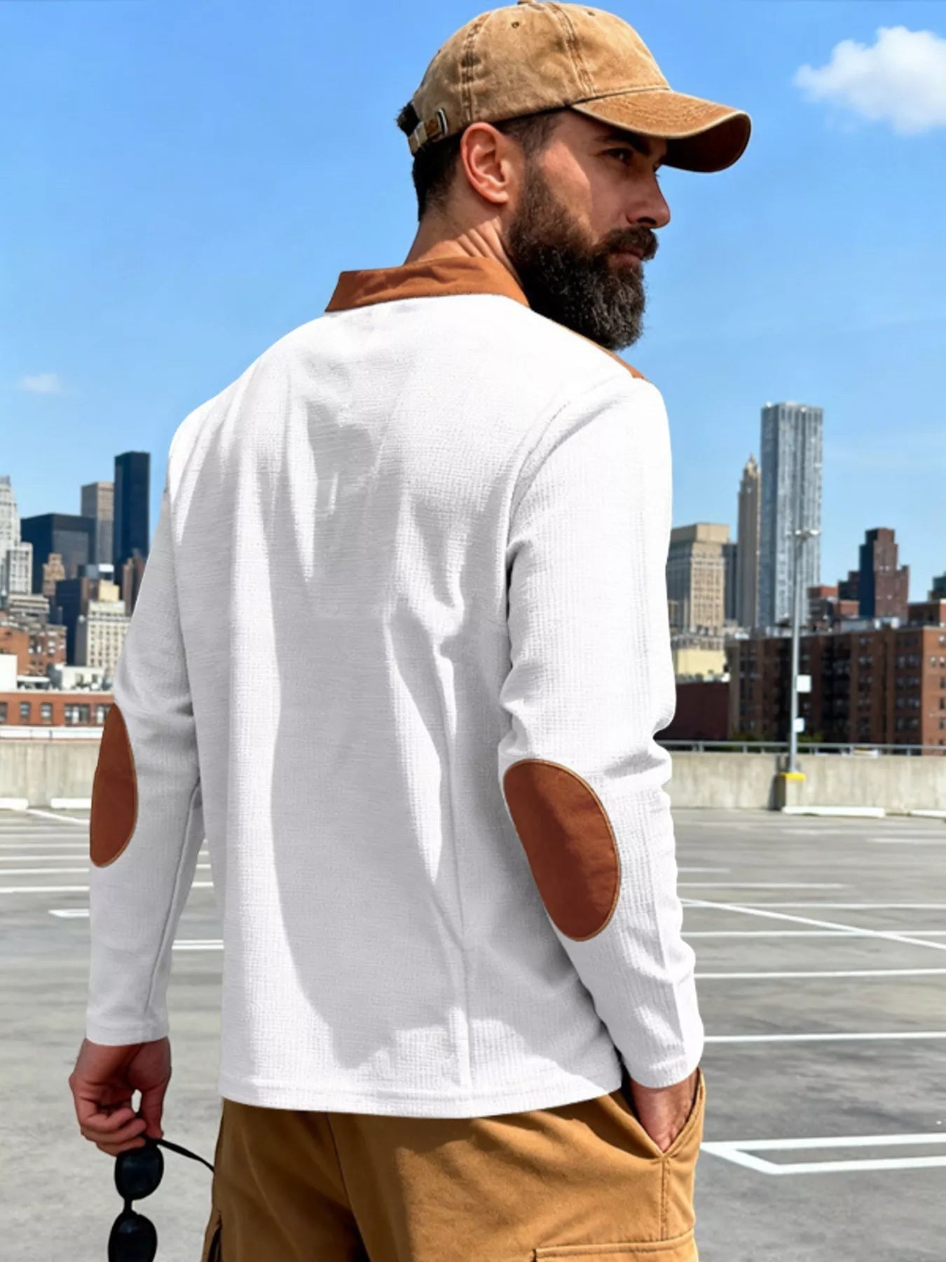 Stylio men's white long sleeve t-shirt with brown elbow patches and lace-up detail. Model wears a brown cap and tan cargo pants.